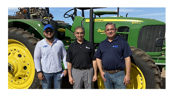 Three men standing in front of a John Deere tractor