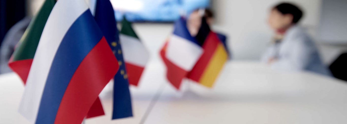 Multiple flags on a table with people meeting in background. 