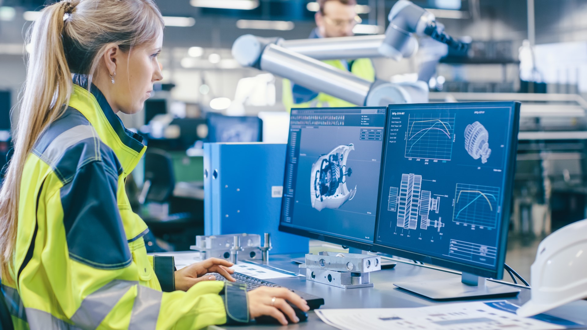 Woman wearing a yellow work jacket is using a computer to design an engine or rotor