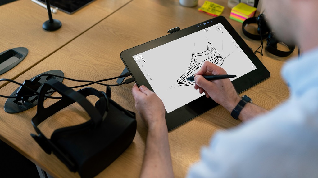 Man using hand to draw on a tablet computer screen with a virtual reality headset on the table next to him.