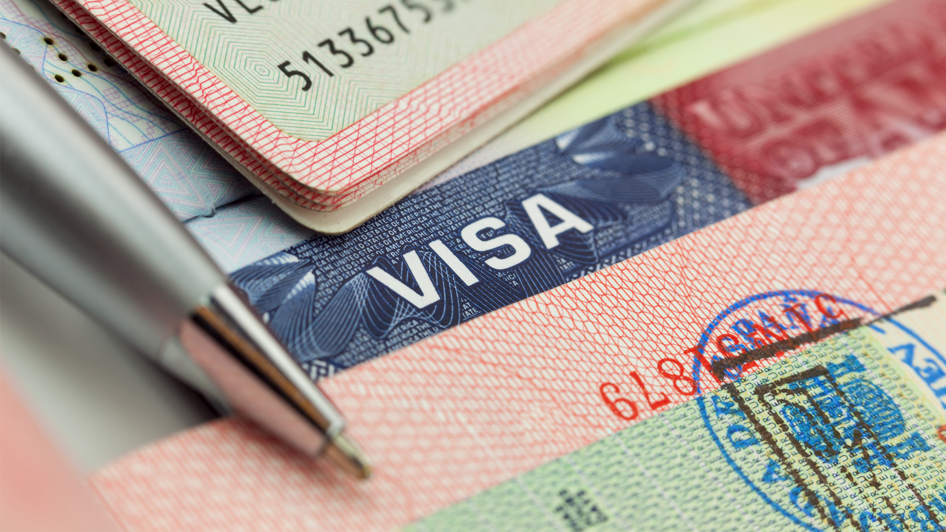 Different visas and stamps in a passport travel background with pen image