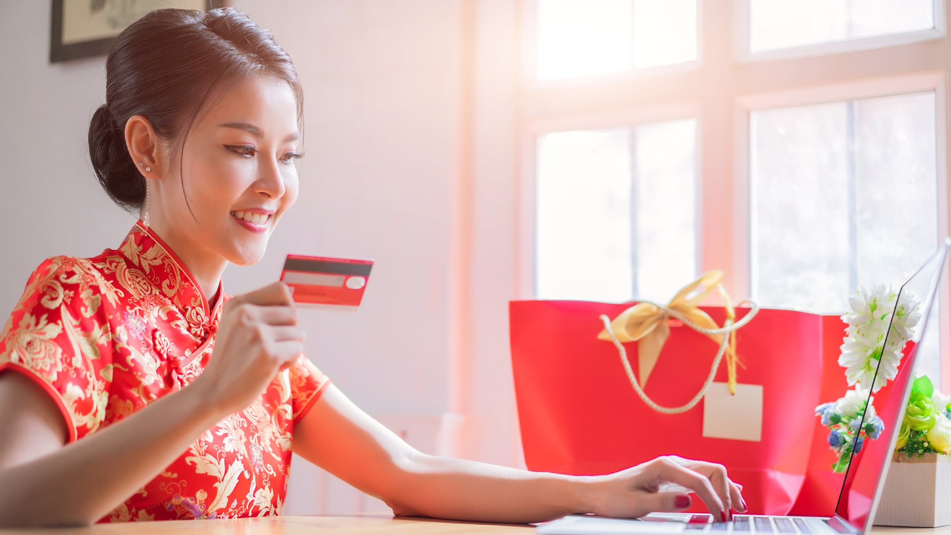 Happy chinese woman wearing a qipao dress traditional or cheongsam and buying online with a red credit card. Online Shopping Website on Laptop