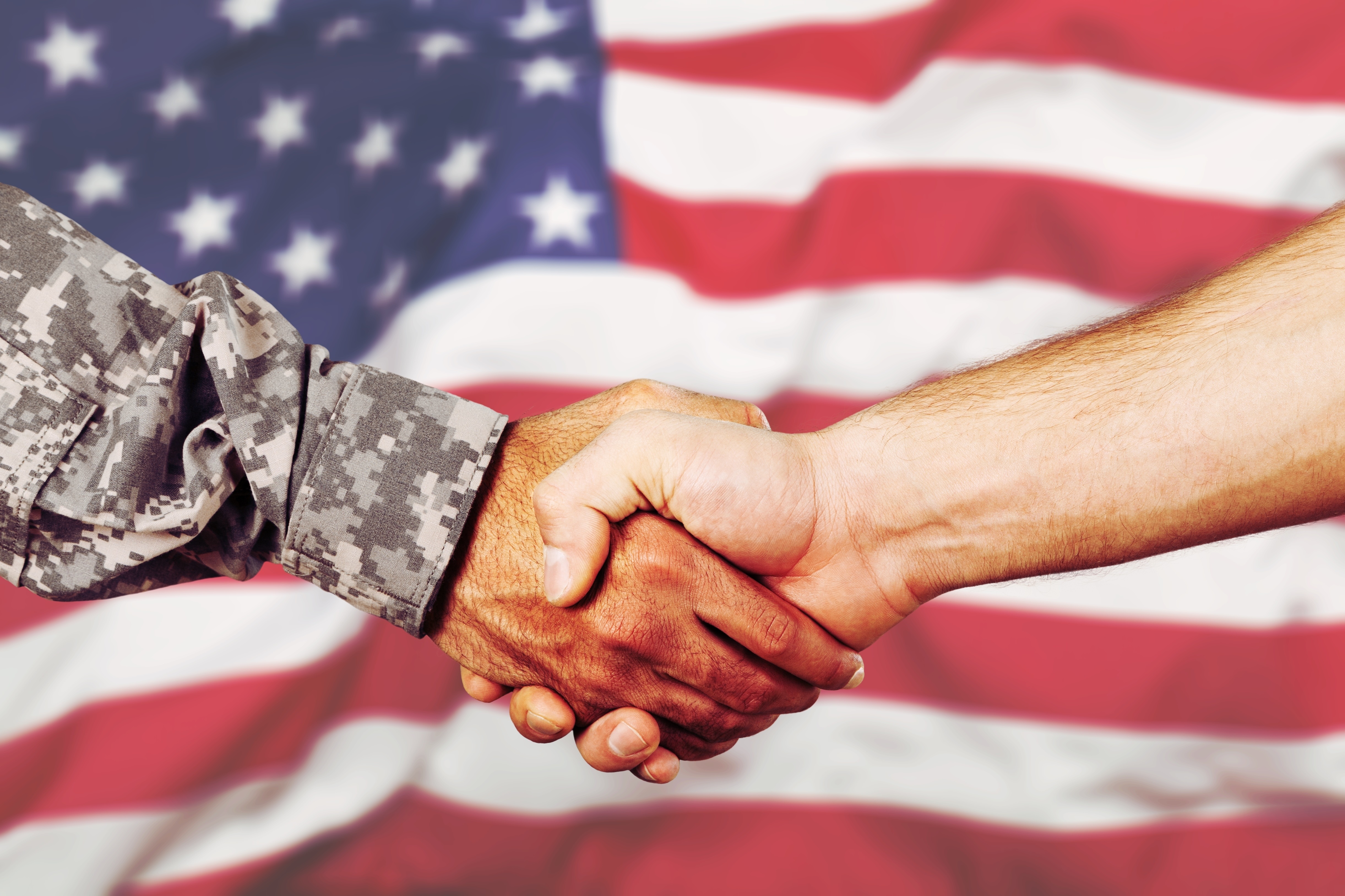 Military veteran shaking hands with business man in front of American flg