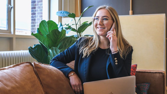 Young woman with glasses sitting on a couch and talking on a phone