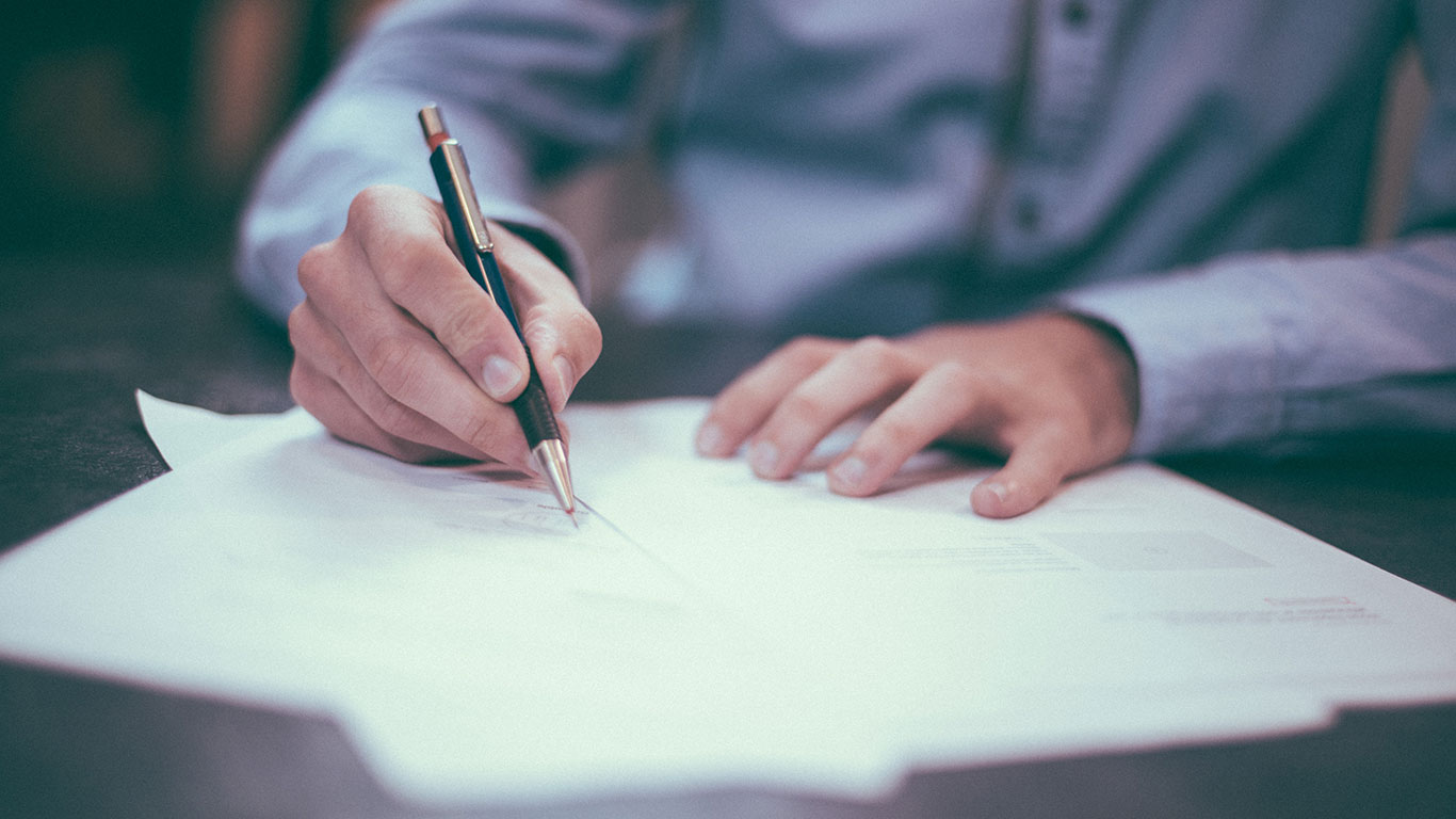 Man wearing blue shirt writing on paper on a desk