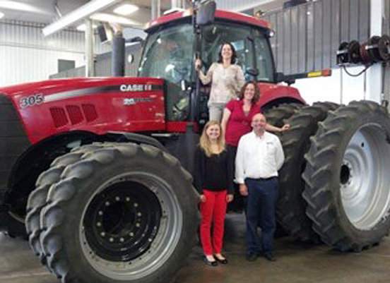 Very large red tractor with four people standing on it and by it