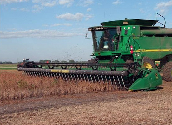 Large Agricultural grain collector plowing a field of wheat during the day