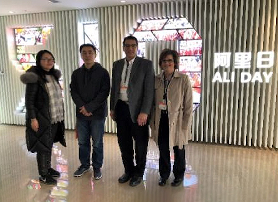 Four people posing for a picture in front of a ALI Day sign