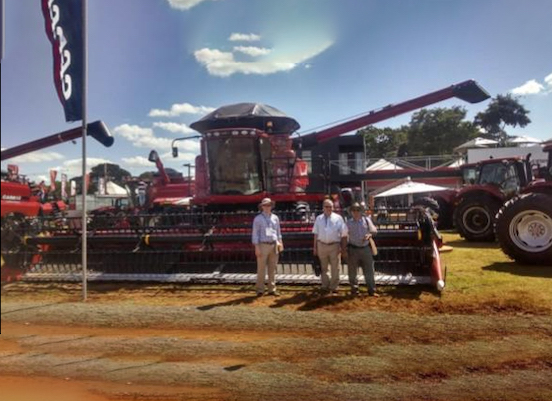 Three people standing in front of a red large farming equipment 