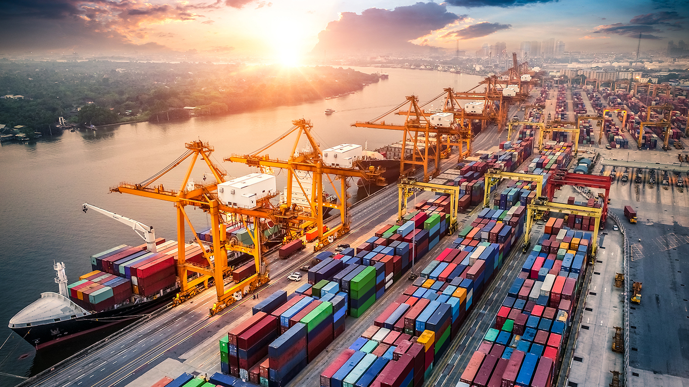 A bird's eye view of a loading dock for cargo ships, the sun on the horizon
