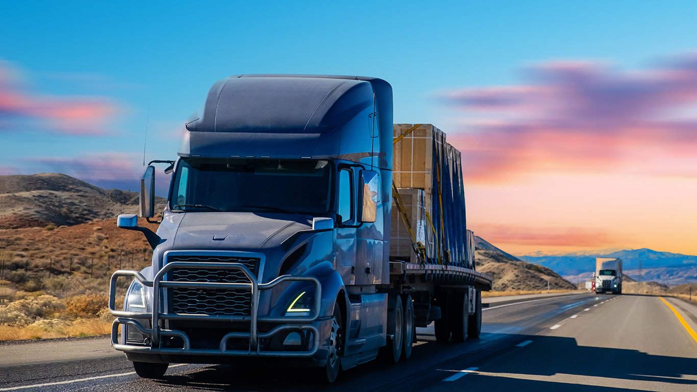 A semitruck hauls cargo, a sunset sky and other trucks in the background