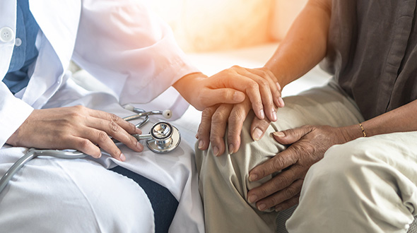 An anonymous doctor places a hand on an anonymous patient's hand in a comforting manner