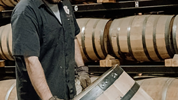 Man wearing black shirt pushing whiskey barrel.