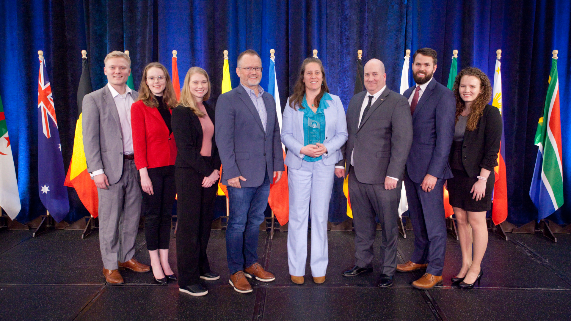 Men and women wearing professional clothing accepting an award in front of flags