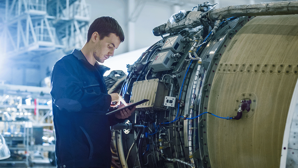 A maintenance person reviews documentation while repairing and aircraft engine