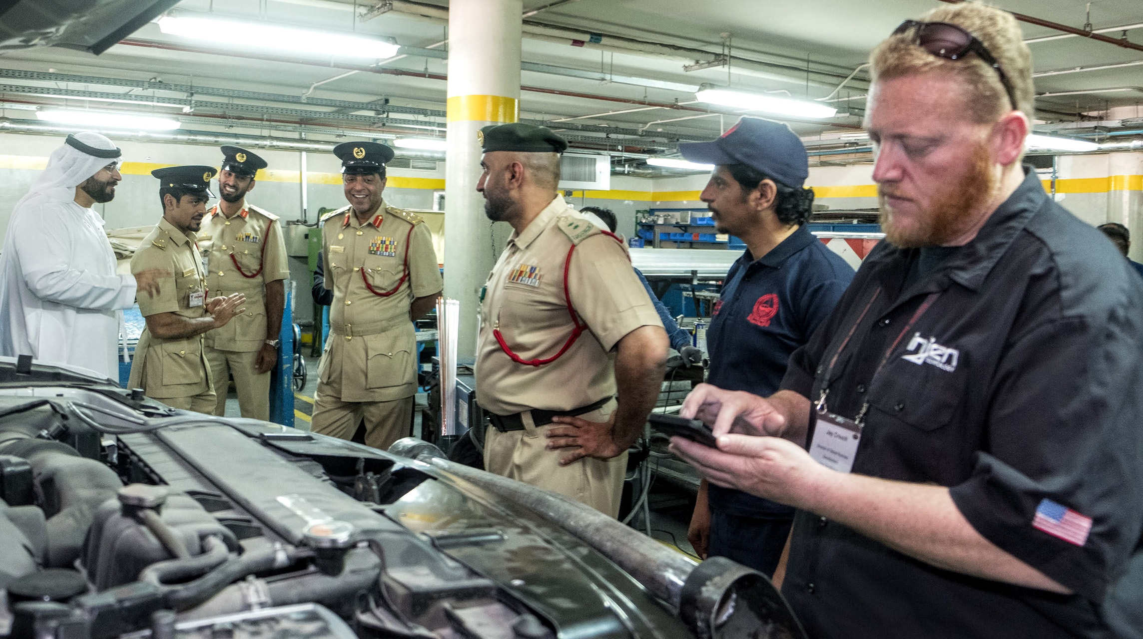 Six men, four Dubai policemen, huddle with mechanics around a vehicle with hood raised.