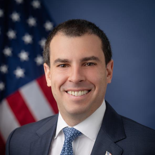 Headshot of Alex Lasry, with U.S. flag in the background.