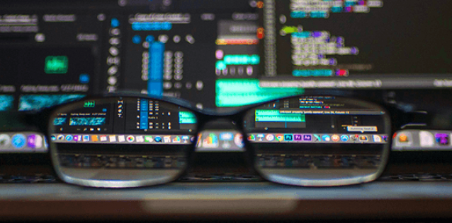 Glasses in the forground with computer screens and coding elements in the backgound