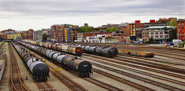 Train yard with trains, rail tracks, and background buildings. 