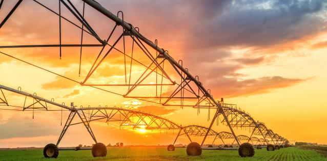 Crop irrigation equipment in a green field with beautiful sunset in background