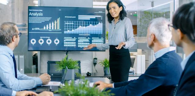 A woman briefing men at work with a series of charts behind her