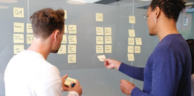 Two people discussing notes posted on a glass wall