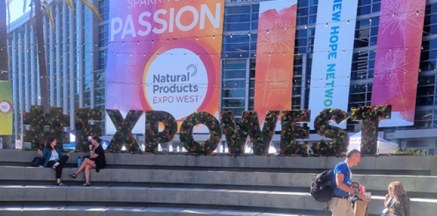 Natural Products Expo West signage on the steps of the convention center with two people