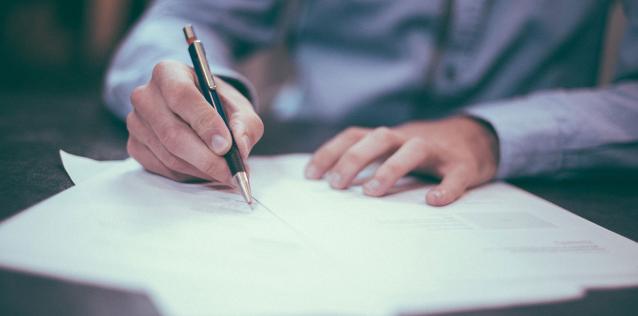 Man wearing blue shirt writing on paper on a desk