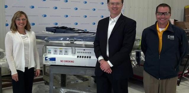 Two men and one woman standing next to a Spectrum Aeromed machine