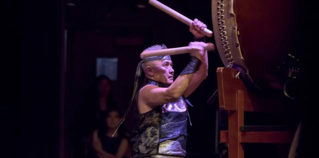 Man on stage striking a hug horizontal drum