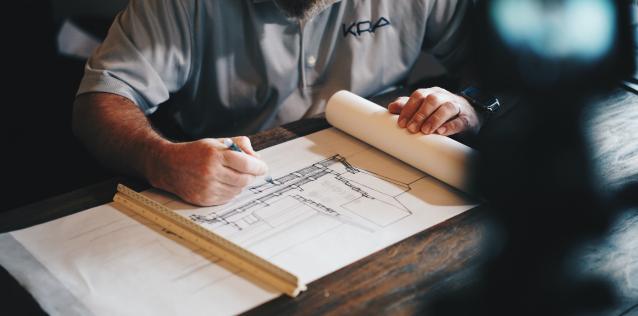 Man sketching architectural blueprints on a table with design tools