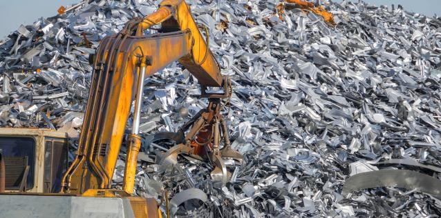 A construction crane is shown reaching into a large mound of scrap metal