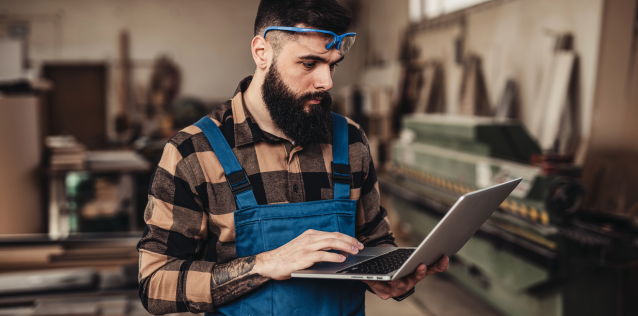 Man in overalls works on laptop, small business owner.