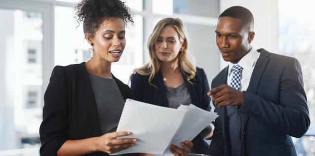 Three people in business attire are looking over some files.
