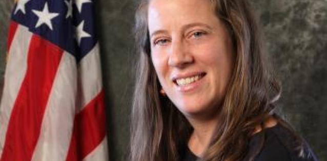 Woman with long brown hair sitting in front of U.S. flag