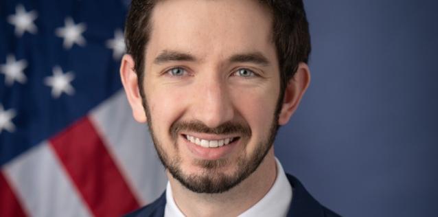 Photo of Christopher Abbot against a blue background with an American flag.