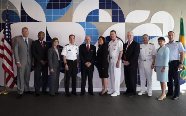 Group of military women and men posing for picture besides U.S. flag and organization flag 