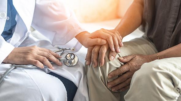 An anonymous doctor places a hand on an anonymous patient's hand in a comforting manner