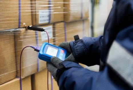 Hand of worker using a thermometer to measure the temperature of goods in cargo boxes