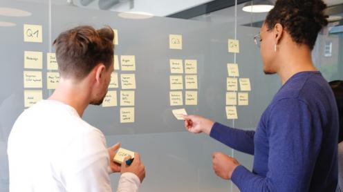 Two people discussing notes posted on a glass wall