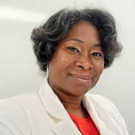 Bust photo of Crystal Mills with a blurred off-white background wearing an orange blazer with an orange blouse underneath.