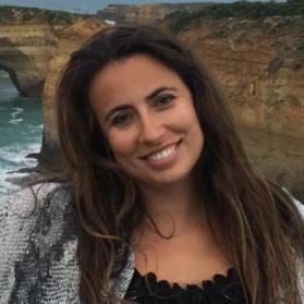 Bust photo of Emily Gereffi in front of a water filled canyon, wearing a two-toned grey Greg Sizemore wearing a black blazer, white collared shirt, and grey poncho over a black blouse.