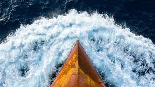 The bow of a cargo ship cuts through dark water