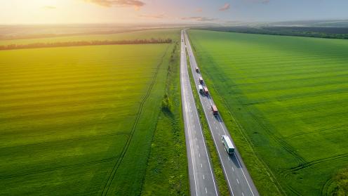Two lush fields are separated by a highway with semitrucks hauling freight.